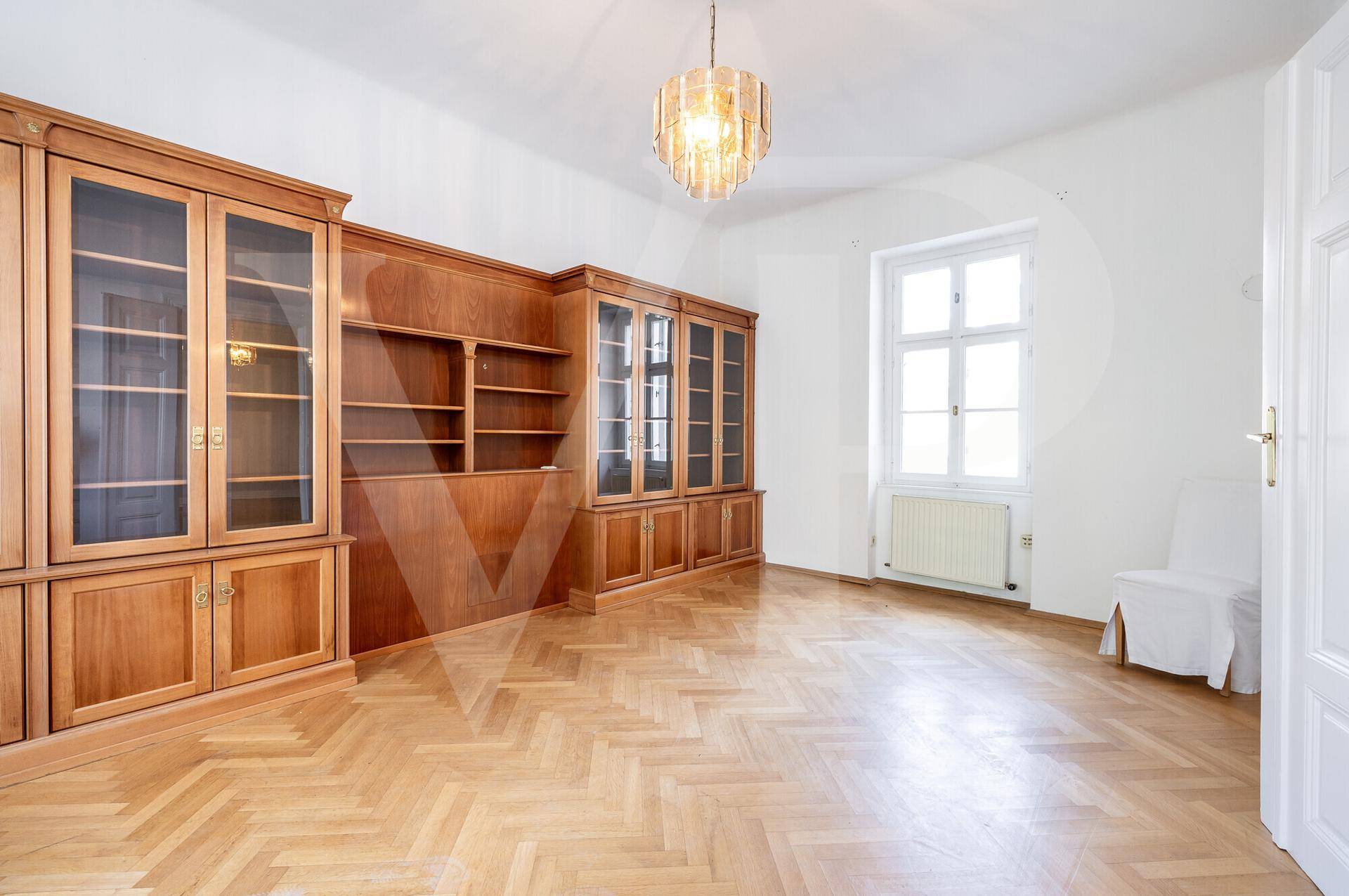 Geräumiges Zimmer mit Fischgrätparkett und einer großen, eingebauten Bücherwand aus Holz.