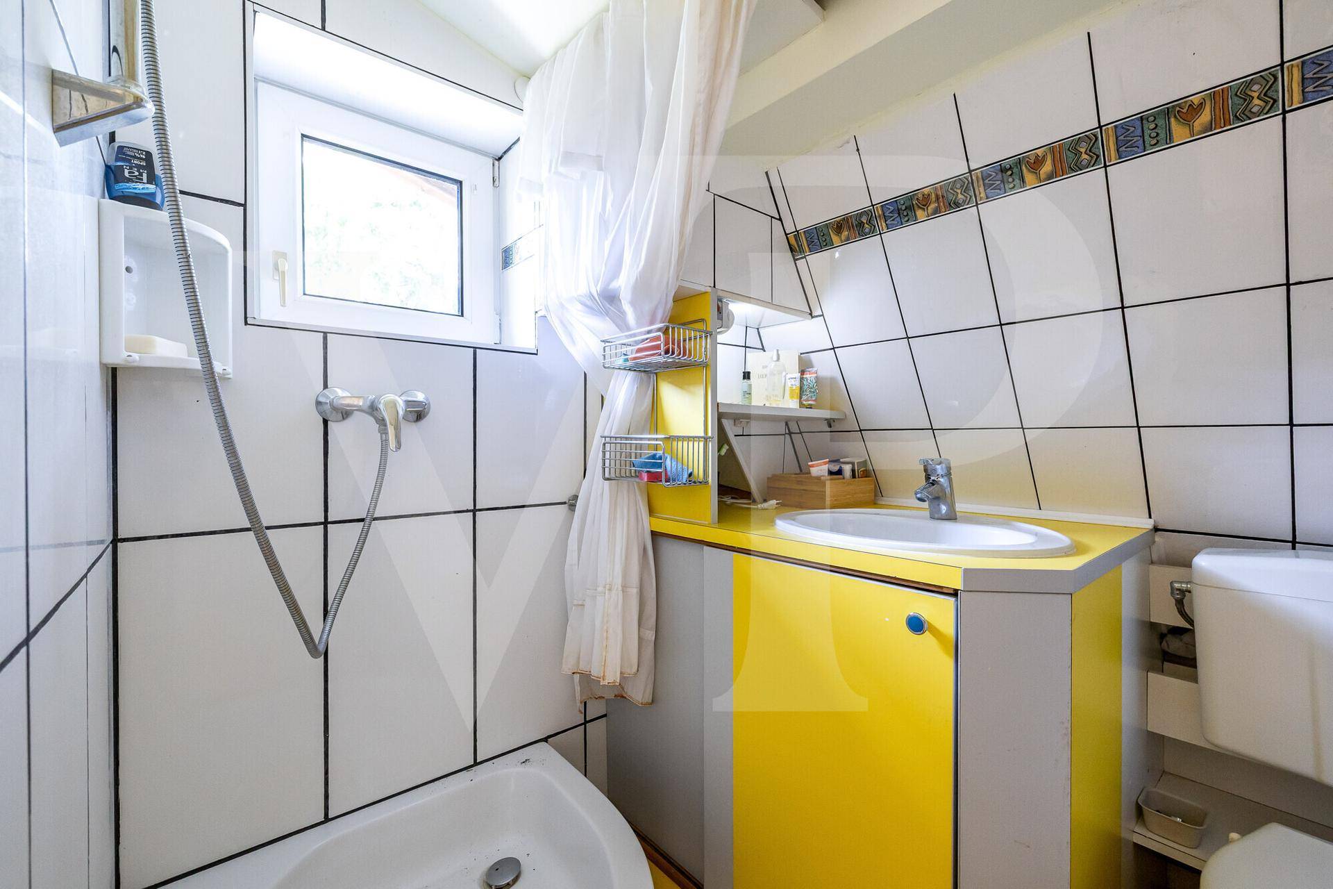 Helles Badezimmer mit Badewanne, Duschvorrichtung, gelbem Waschtisch und Fenster für Tageslicht.