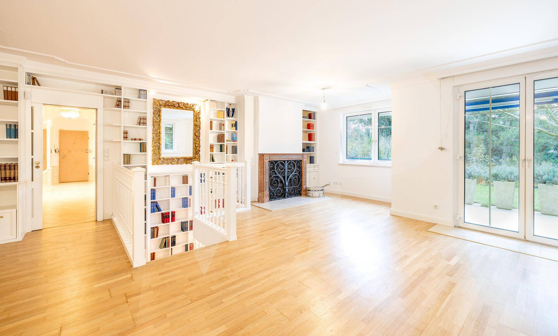 Helles Wohnzimmer mit Parkettboden, Einbauregalen und einem dekorativen Kamin, mit Zugang zum Garten.