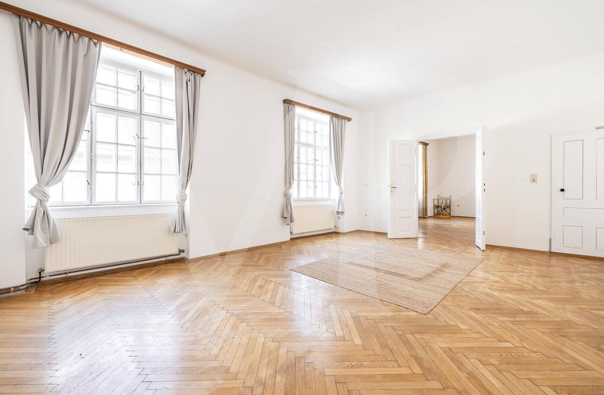 Großes, helles Zimmer mit Fischgrätparkett, hohen Fenstern und viel Tageslicht.