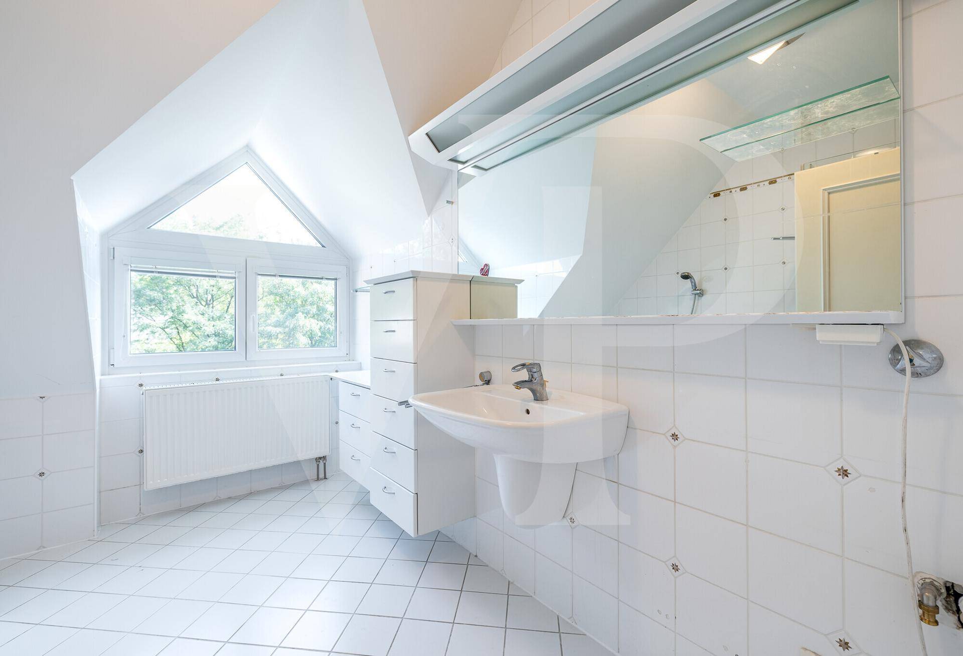 Helles Badezimmer mit weißen Fliesen, Waschbecken, großem Spiegel und Fenster im Dachgeschoss.
