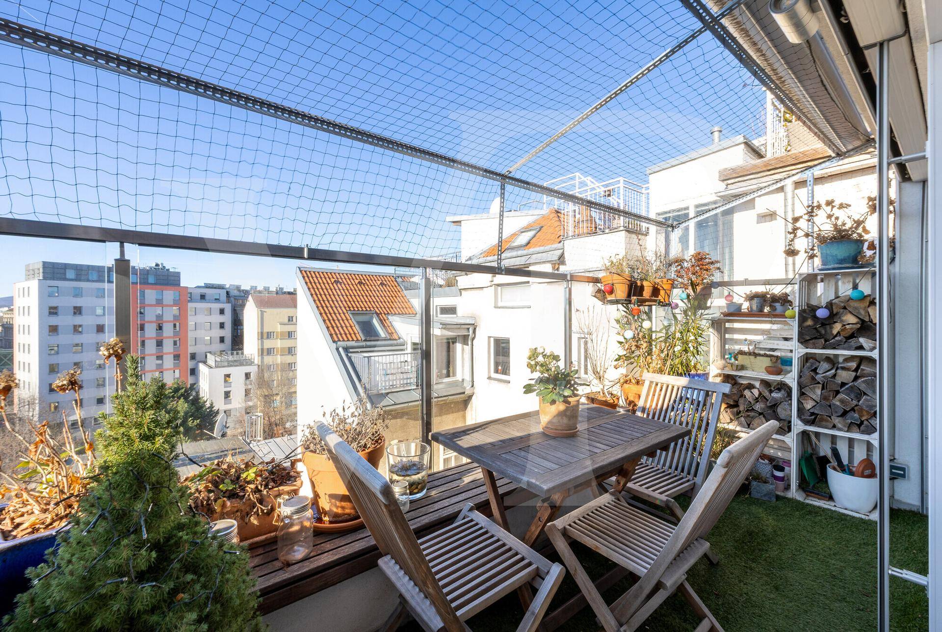 Sonnige Dachterrasse mit Holztisch, Stühlen und weitem Stadtblick.