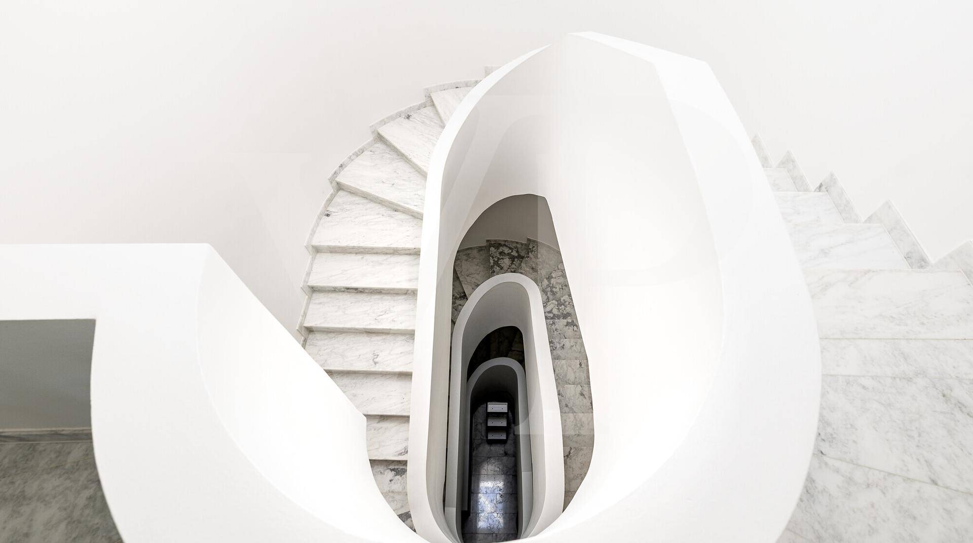 Elegante, geschwungene Marmortreppe mit modernem Design und viel Tageslicht.