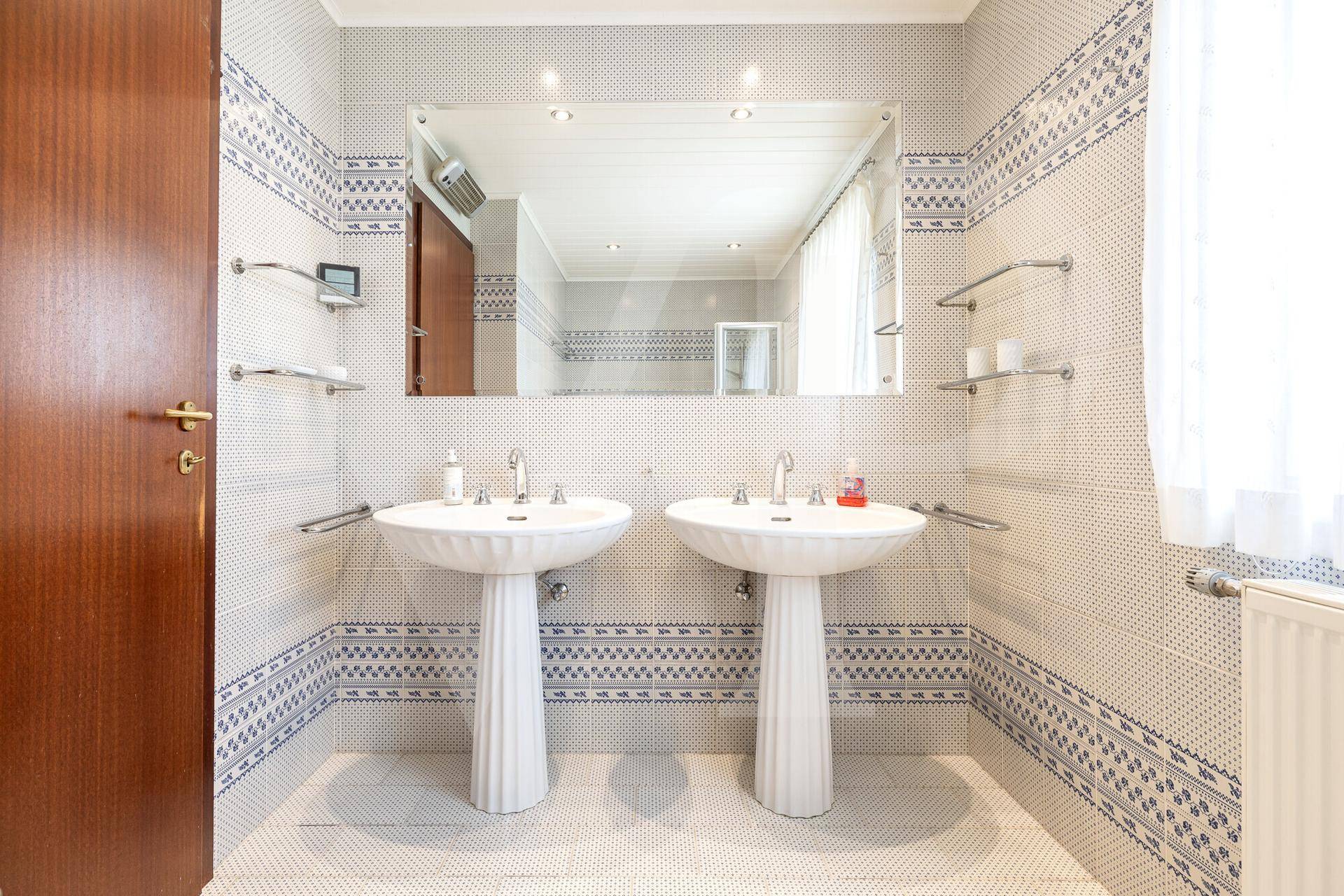 Badezimmer mit zwei Waschbecken, großem Spiegel und dekorativen blau-weißen Fliesen.