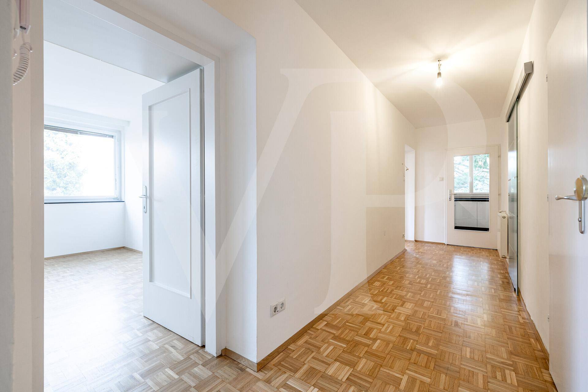 Heller Flur mit Fischgrätparkett und weißen Wänden, der zu weiteren Zimmern führt.