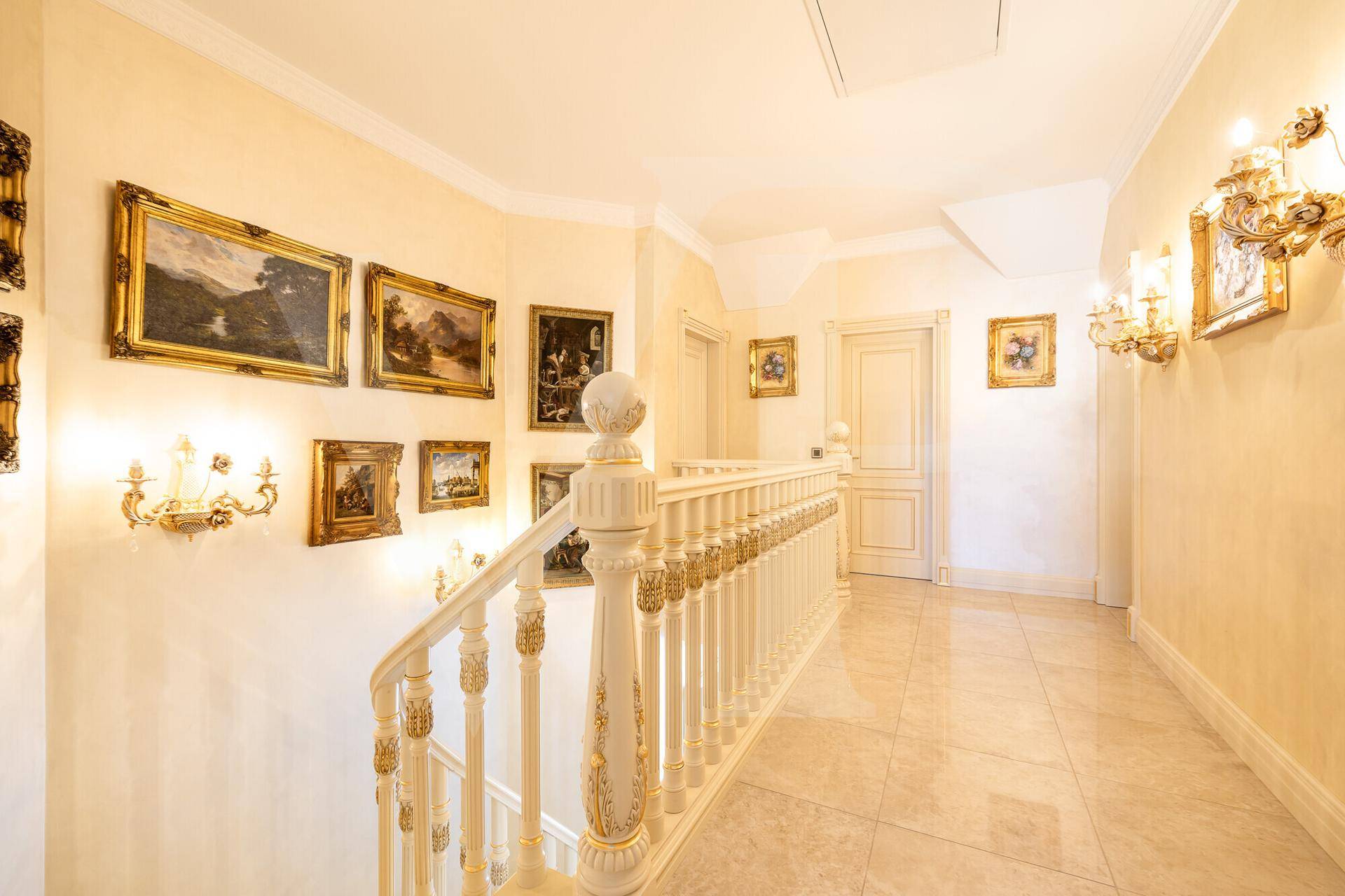 Heller Flur im Obergeschoss mit eleganter Treppe, Kunstwerken und glänzenden Fliesen.