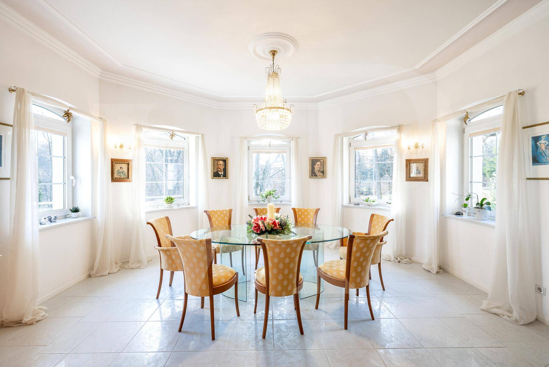 Eleganter Essbereich mit rundem Glastisch, stilvollen Stühlen und vielen Fenstern.