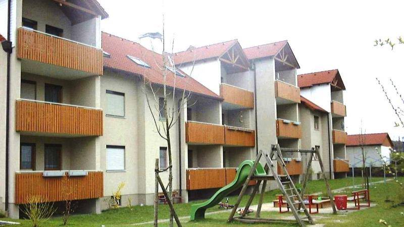 Rückseite eines Mehrfamilienhauses mit zahlreichen Balkonen und einem Kinderspielplatz im Vordergrund.