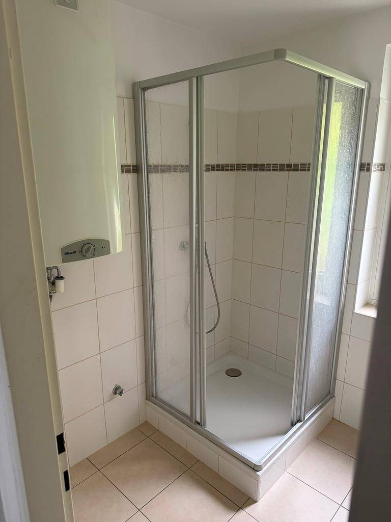 Helles Badezimmer mit Duschkabine, weißen Fliesen und einem Warmwasserbereiter.