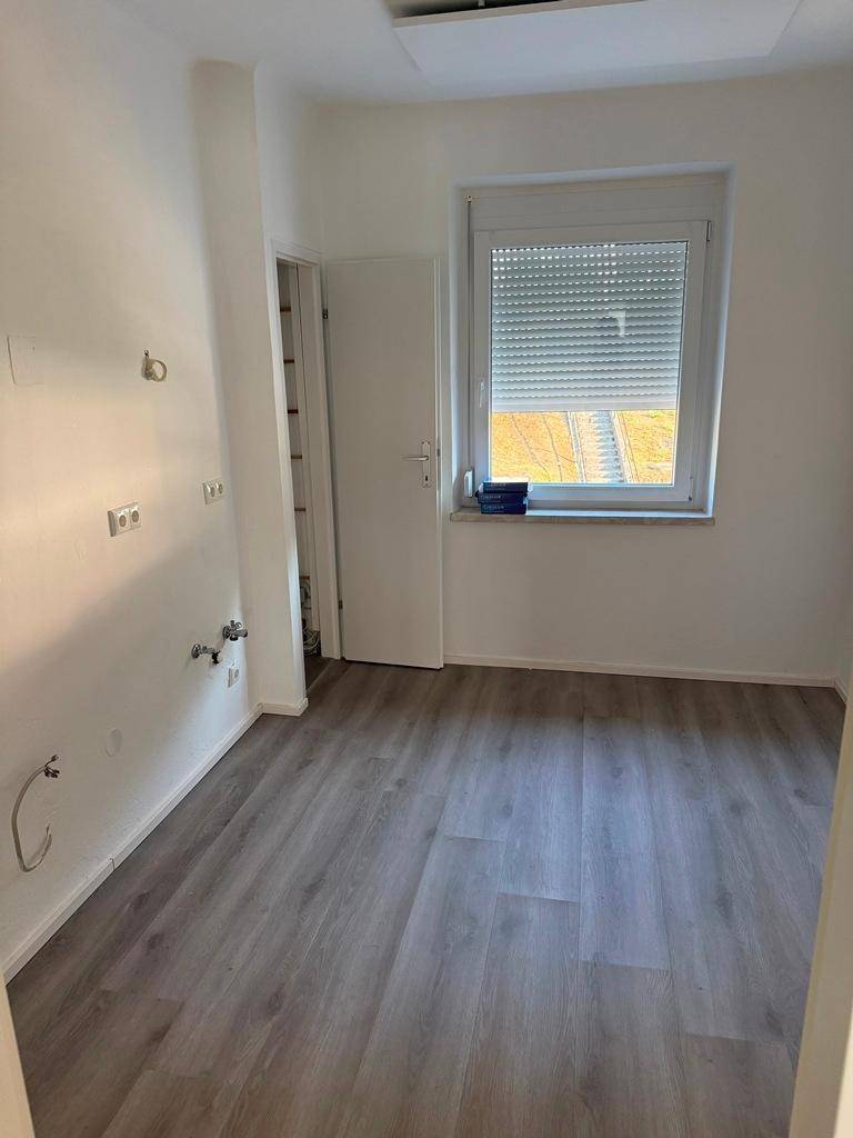 Leere Küche mit Anschlüssen für Spüle und Geräte, hellem Boden und Fenster.
