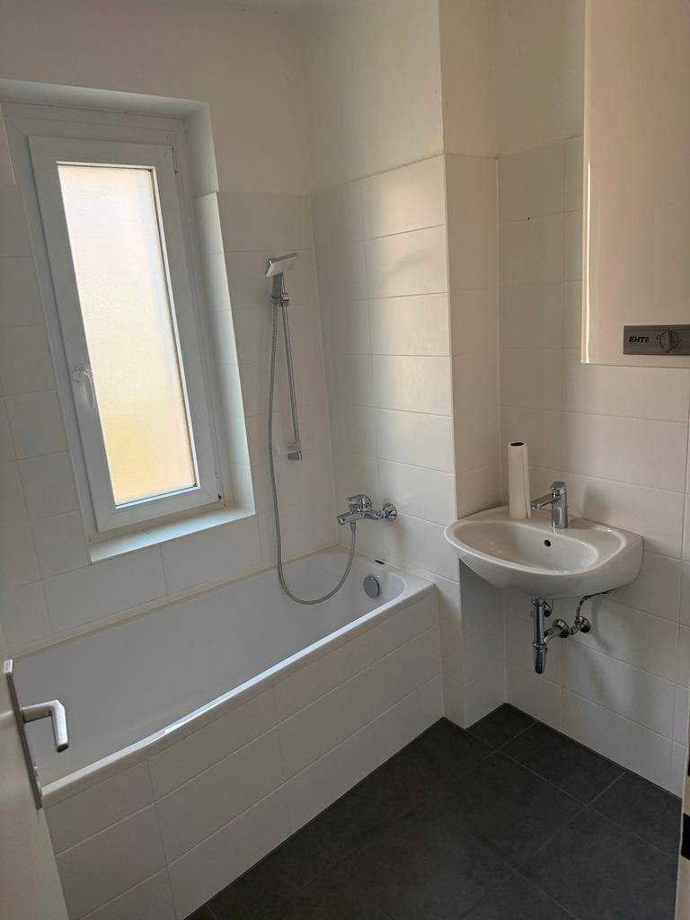 Modernes Badezimmer mit Badewanne, Waschbecken und einem Fenster für Tageslicht.
