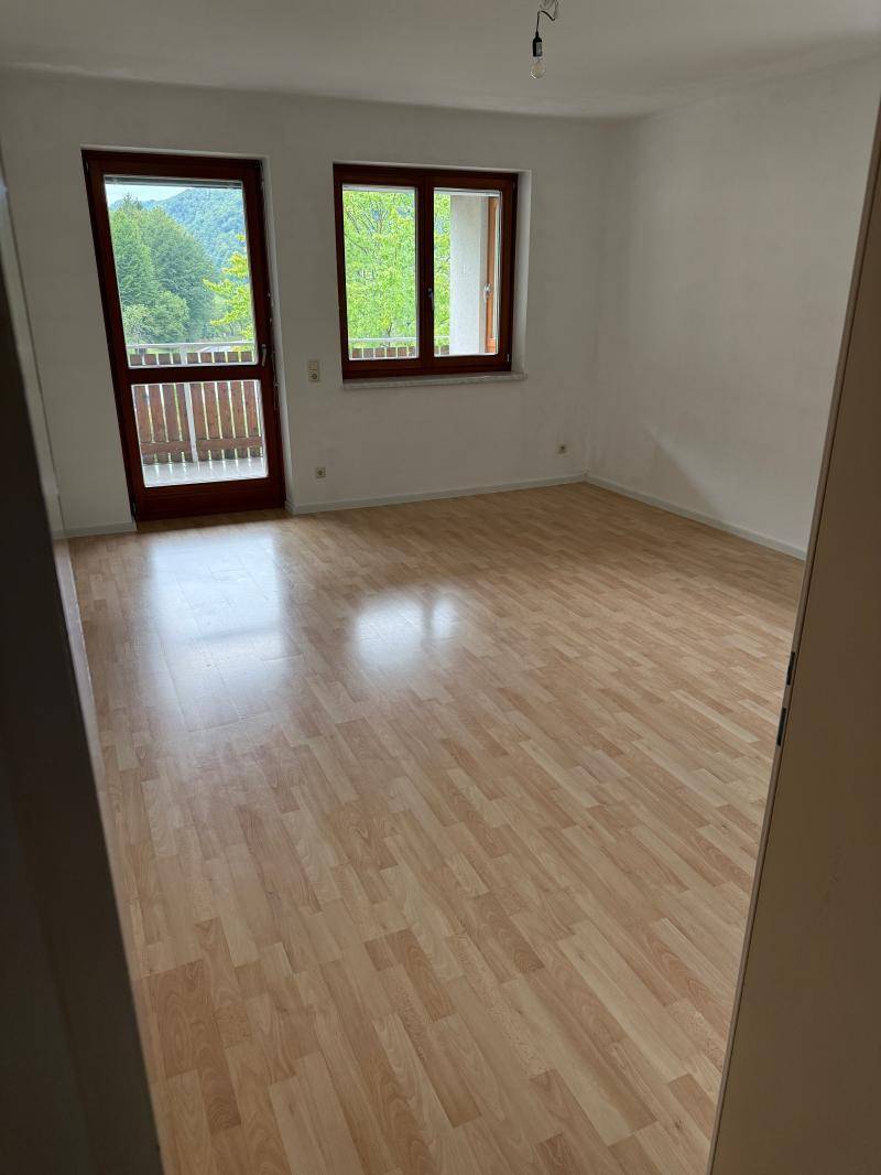 Leeres Zimmer mit Laminatboden, weißen Wänden und Zugang zu einem kleinen Balkon.