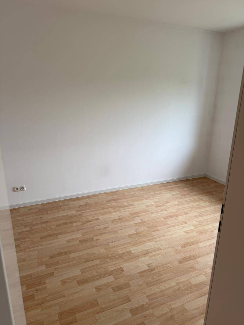 Helles, leeres Zimmer mit Laminatboden und weißen Wänden, bereit zur Einrichtung.