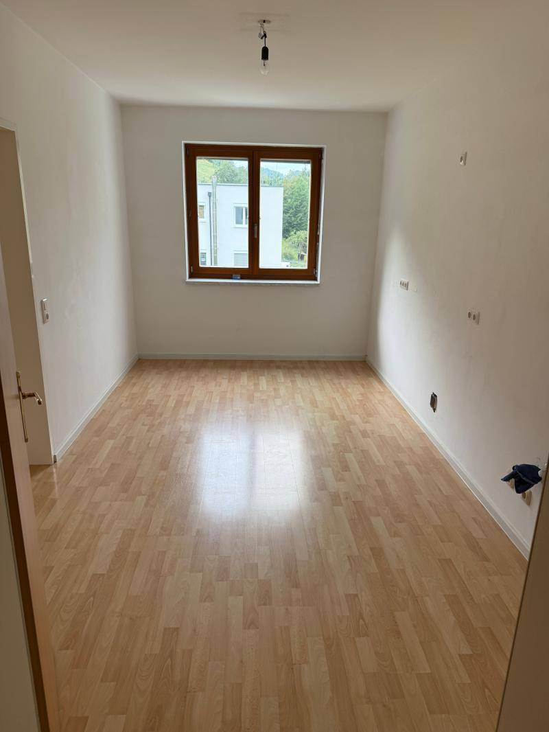 Leeres Zimmer mit Laminatboden und einem Fenster, das viel Tageslicht hereinlässt.