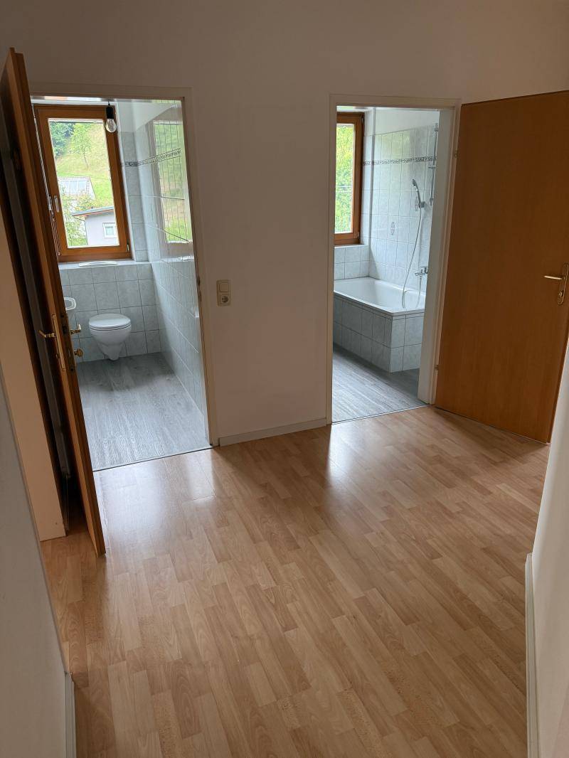 Flur mit Laminatboden und Zugängen zu einem WC und einem Badezimmer mit Badewanne.