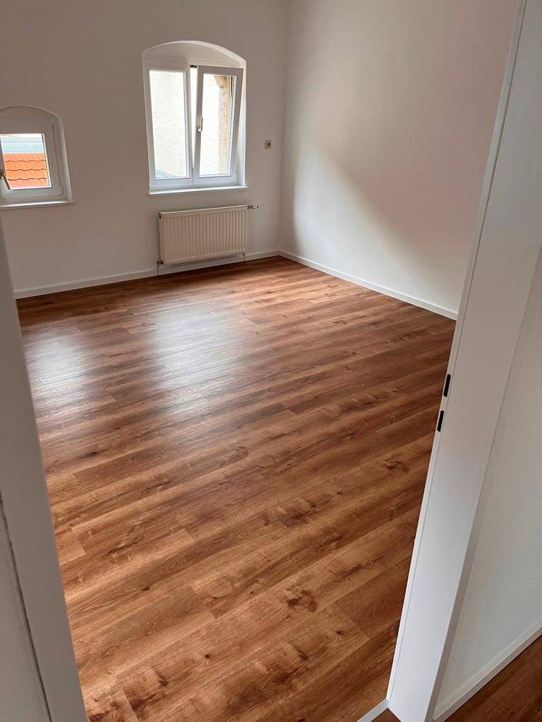 Heller Raum mit neuem Laminatboden und weißen Wänden, bereit für die individuelle Gestaltung.