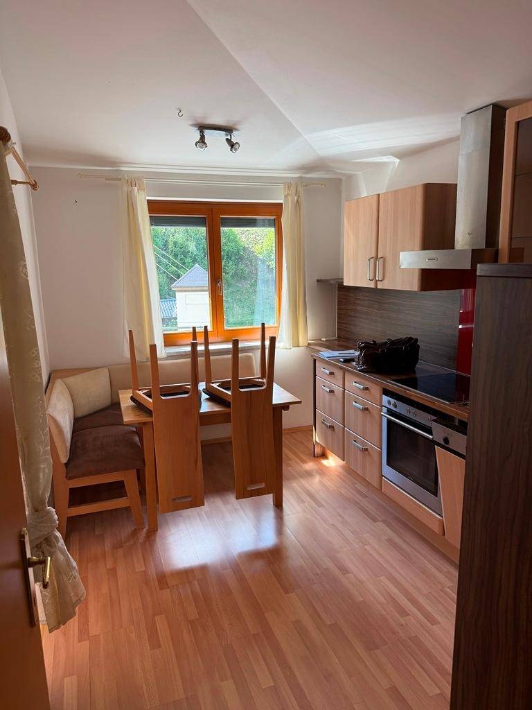 Funktionale Küche mit Holzelementen, Essbereich und Fenster mit Blick ins Grüne.
