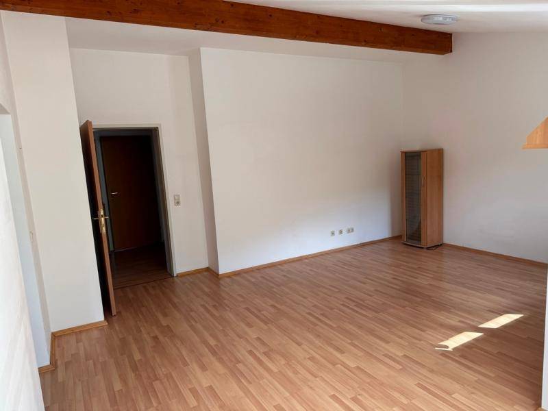 Geräumiges Wohnzimmer mit Laminatboden und sichtbaren Holzdeckenbalken.