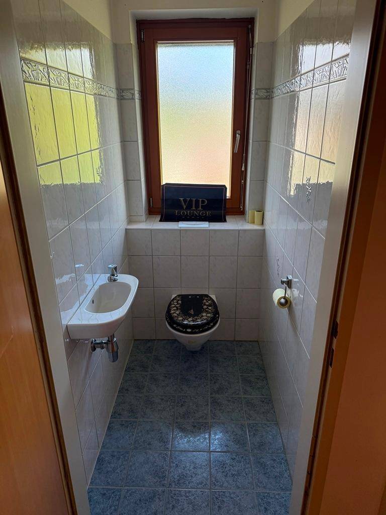 Kleines Gäste-WC mit Fenster, Toilette und Handwaschbecken in hellen Fliesen.