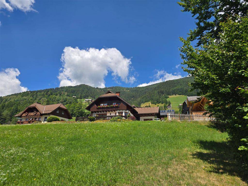Traditionelle Häuser mit Holzbalkonen und Blumenkästen in einer sonnigen Berglandschaft.