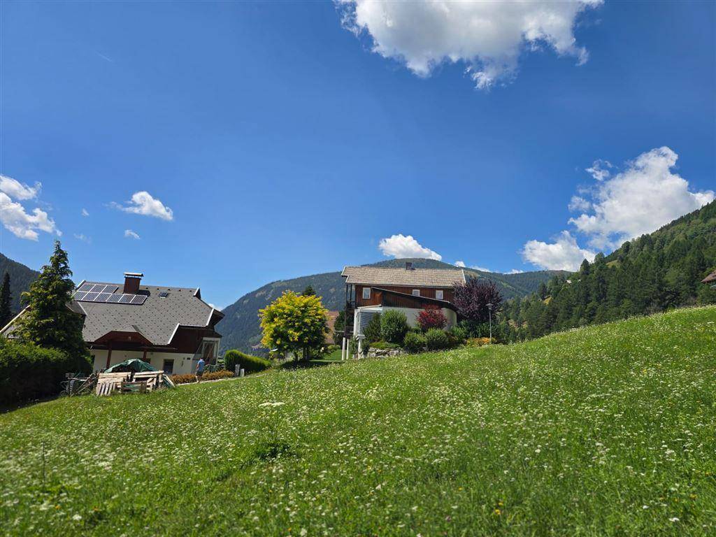 Häuser auf einem Hügel mit grünen Wiesen und einem weiten Blick auf die umliegende Berglandschaft.