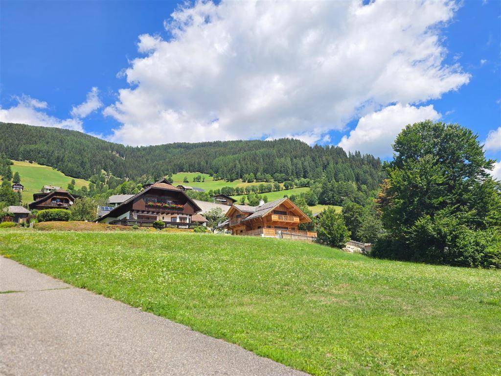 Grüne Wiesen und traditionelle Häuser in einer malerischen Bergkulisse mit einem sonnigen Himmel.