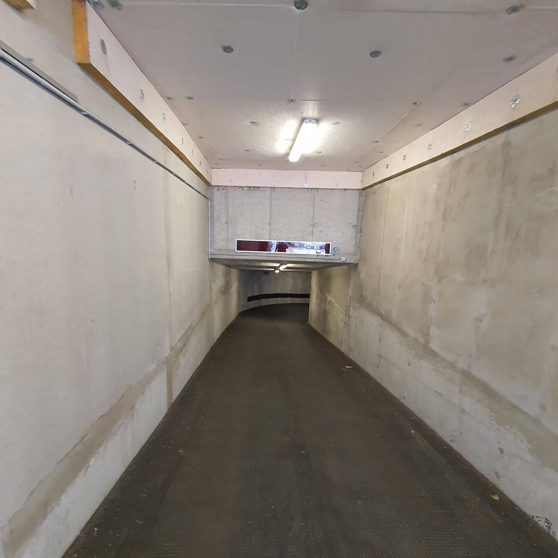 Zufahrtsrampe zu einer Tiefgarage mit Betonwänden und Deckenbeleuchtung.