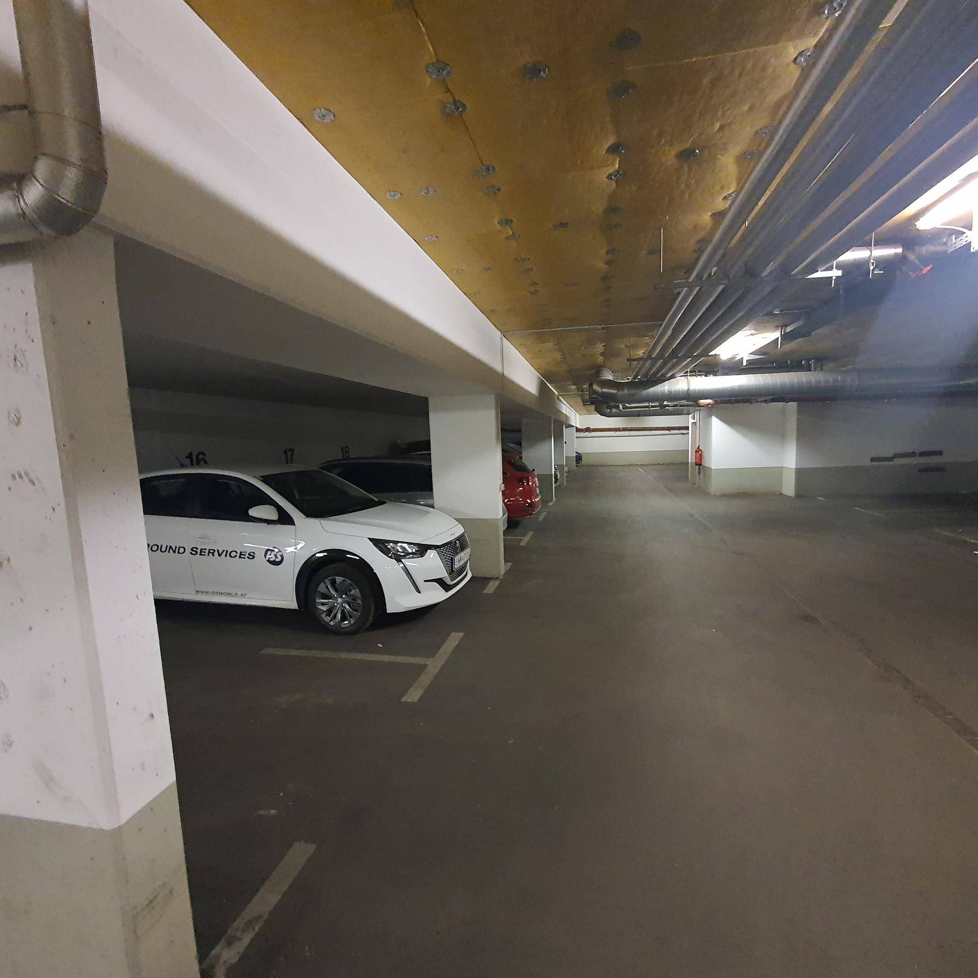 Tiefgarage mit mehreren Stellplätzen, sichtbaren Versorgungsleitungen an der Decke und Betonpfeilern.