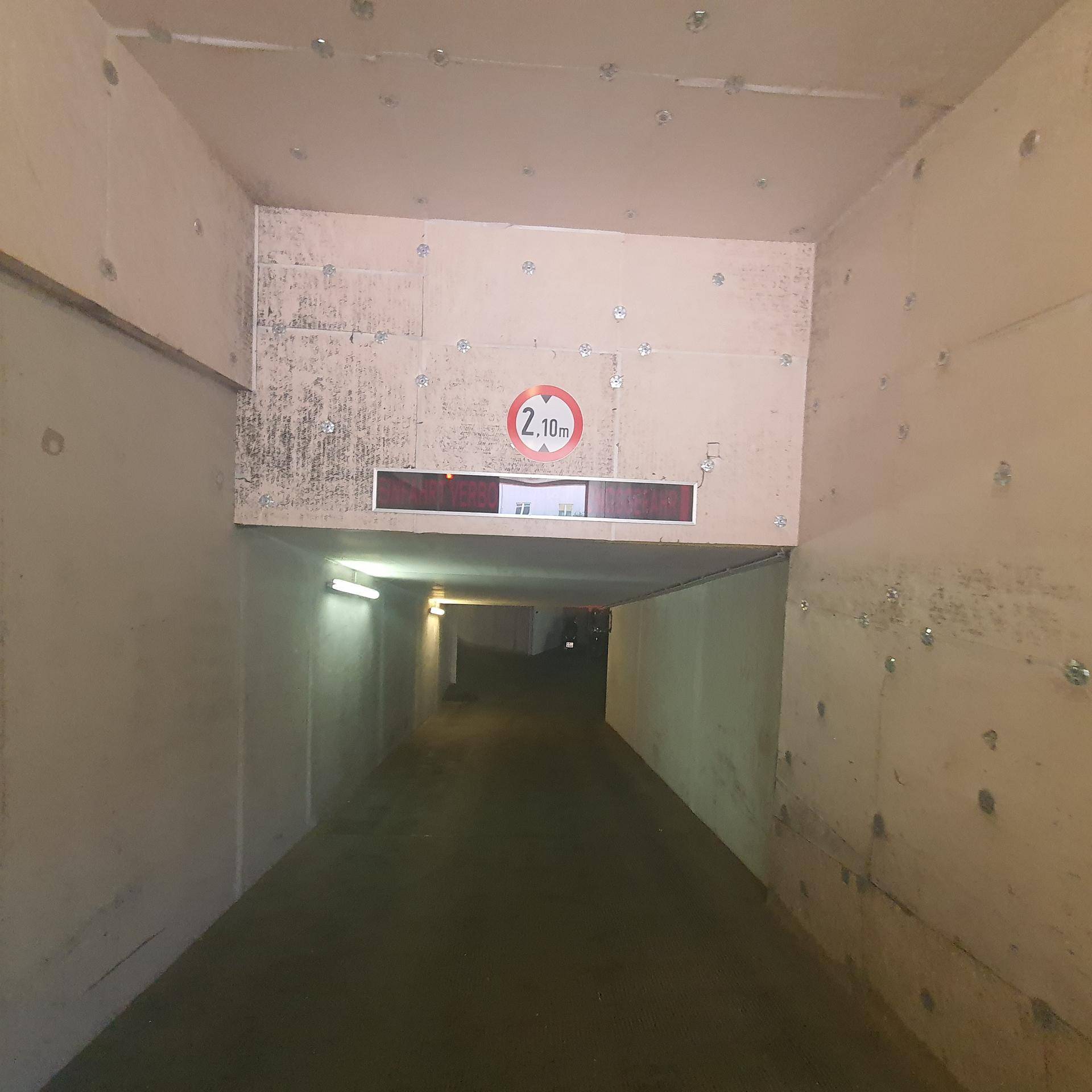 Einfahrtstunnel zu einer Tiefgarage mit Höhenbegrenzung von 2,10 Metern und Betonwänden.