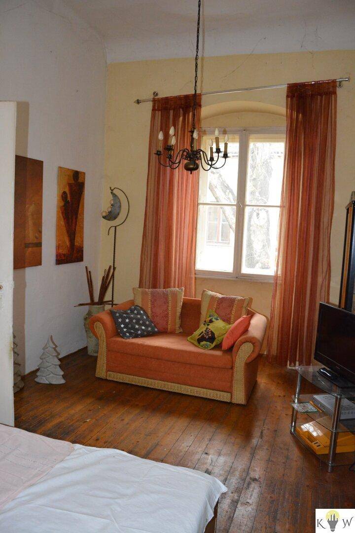 Gemütliches Wohnzimmer mit Holzboden, großem Fenster, einem Sofa und einem Kronleuchter.