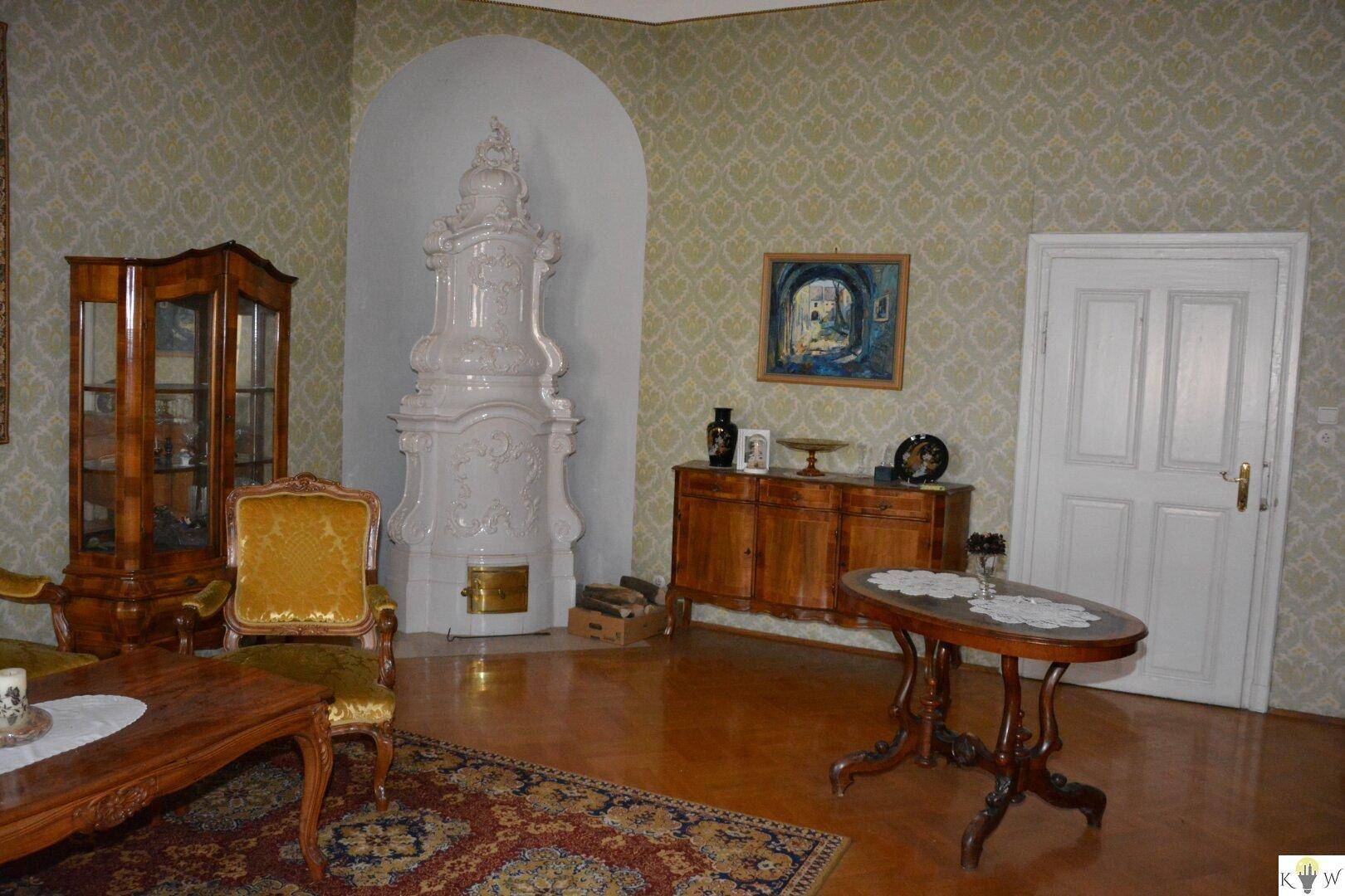 Elegantes Wohnzimmer mit weißem Kachelofen, Parkettboden und antiken Möbeln in traditionellem Stil.