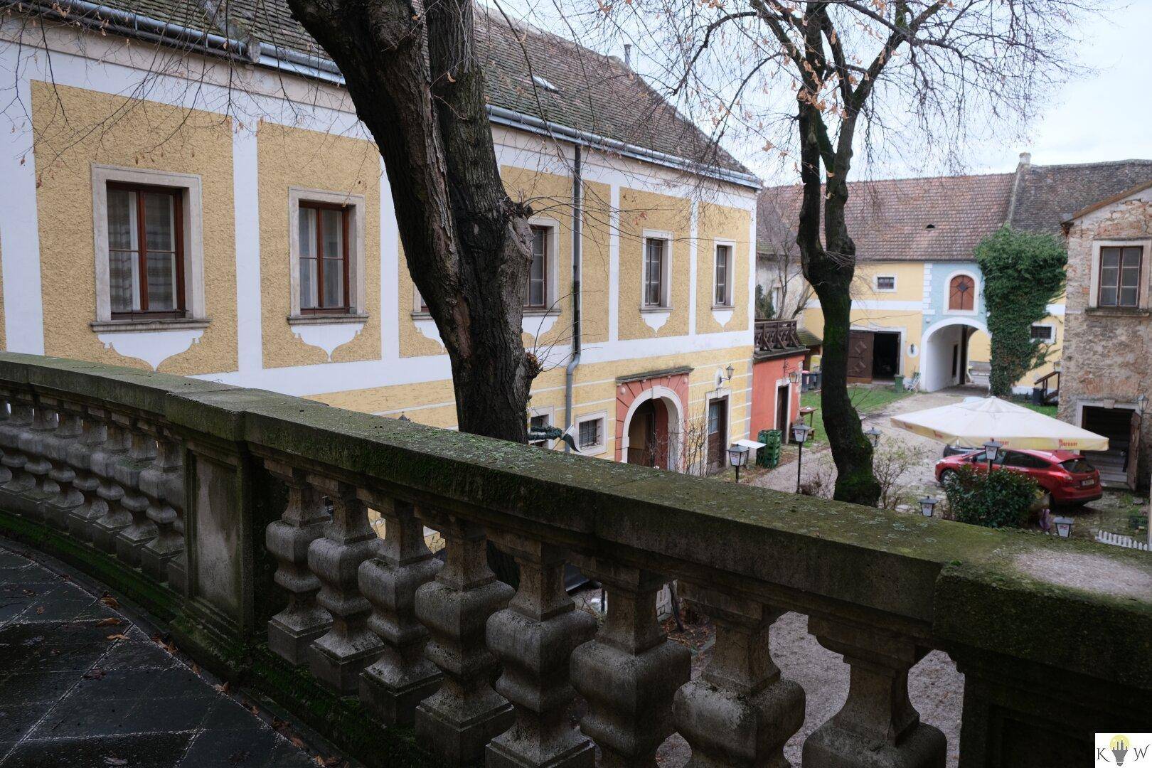 Ansicht eines historischen Innenhofs mit gelben Gebäuden und einer verzierten Steinbalustrade im Vordergrund.