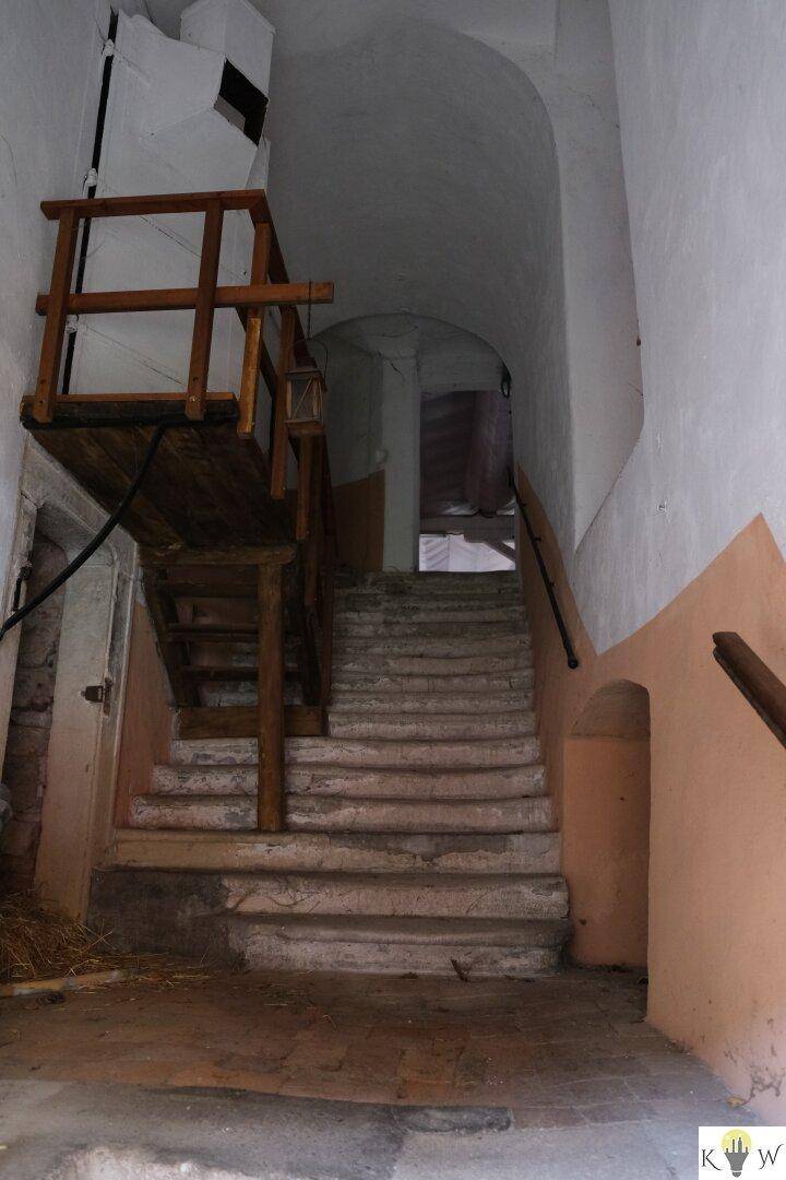 Alter Steintreppenaufgang mit Holzgeländer und gewölbten Wänden in einem historischen Gebäude.