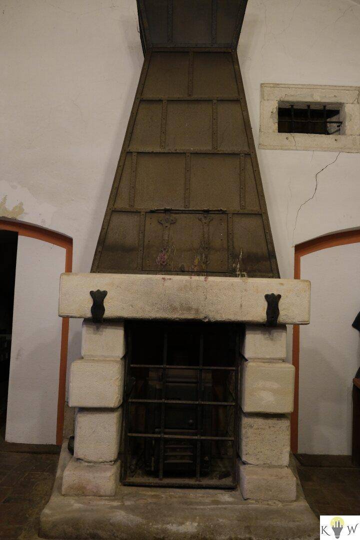Großer, historischer Kamin mit Steinsockel und Metallhaube in einem alten Gebäude.