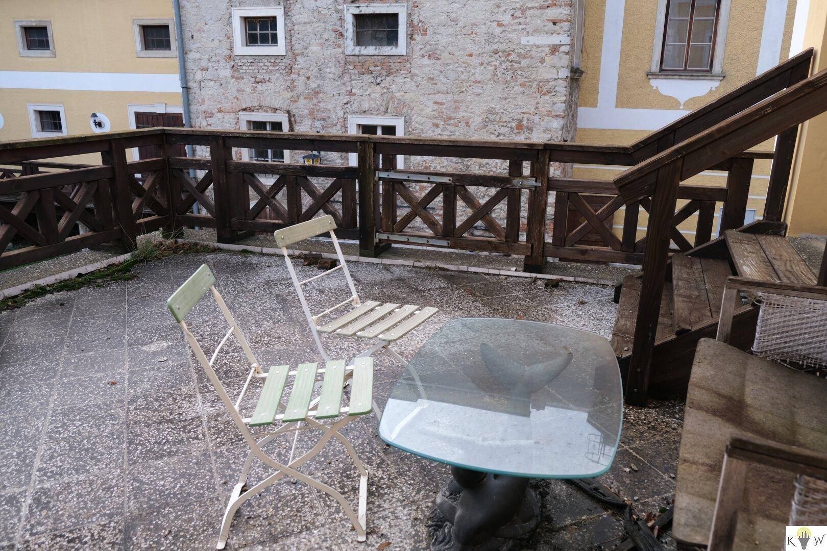 Einfache Außenterrasse mit Tisch und Stühlen, umgeben von historischen Gebäuden im Innenhof.