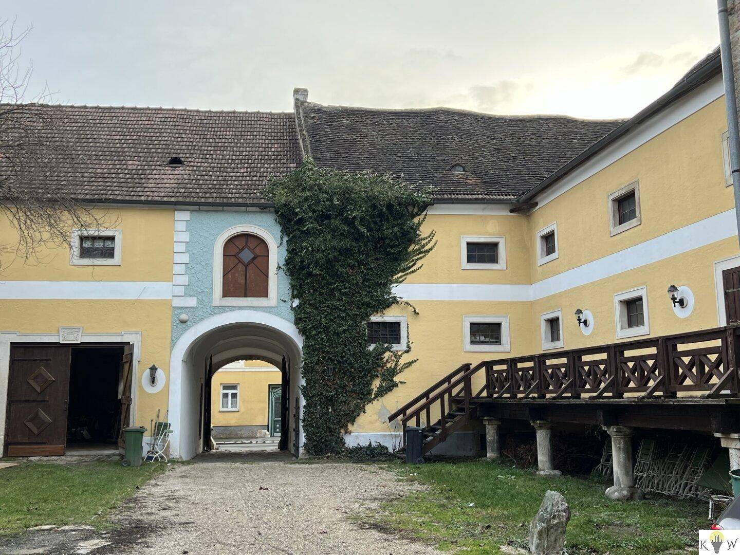 Historisches Gebäude mit gelber Fassade, einem Torbogen und einer hölzernen Brückenkonstruktion im Innenhof.