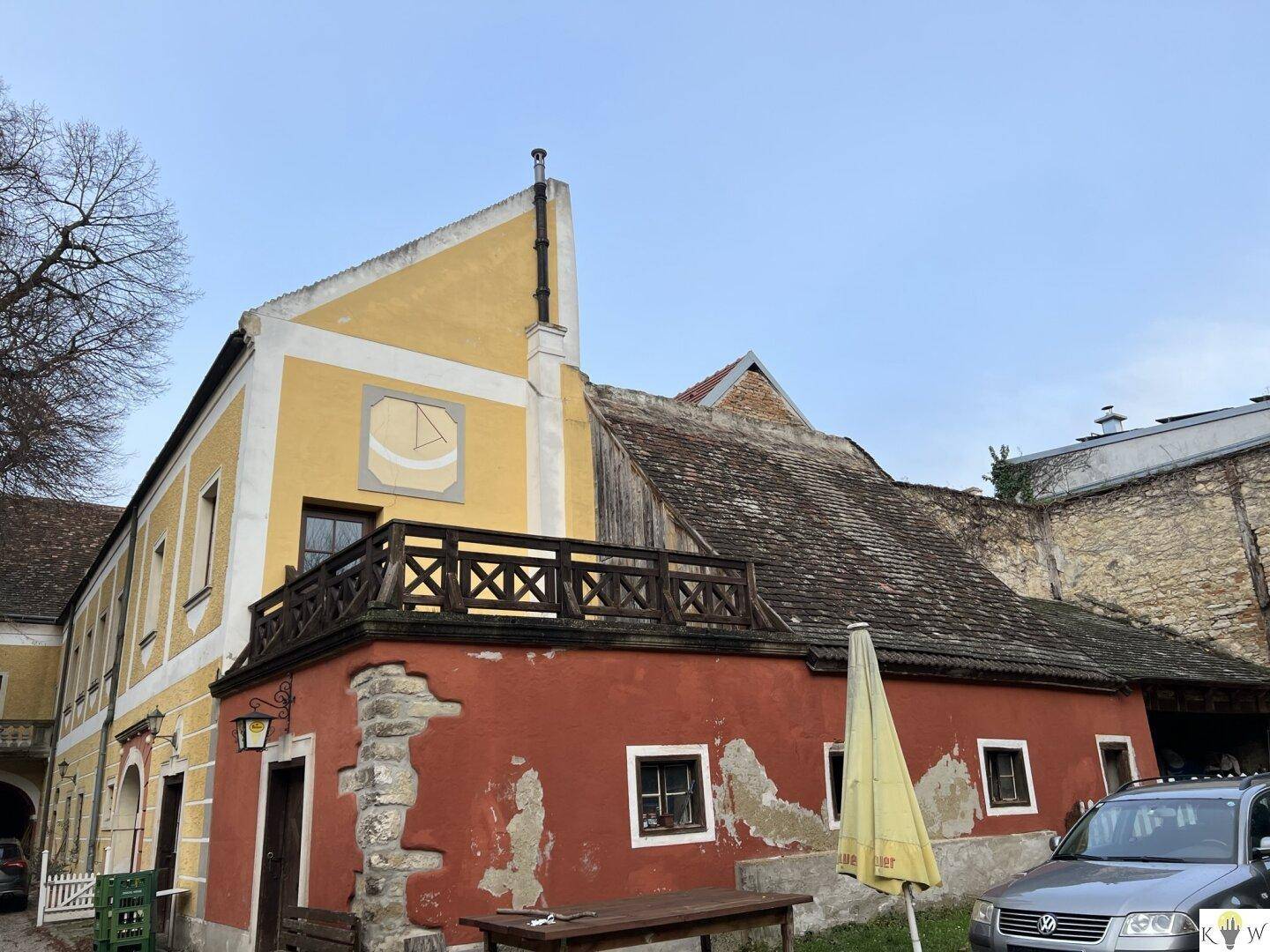 Historisches Gebäude mit roter und gelber Fassade, einem hölzernen Balkon und einer Sonnenuhr.
