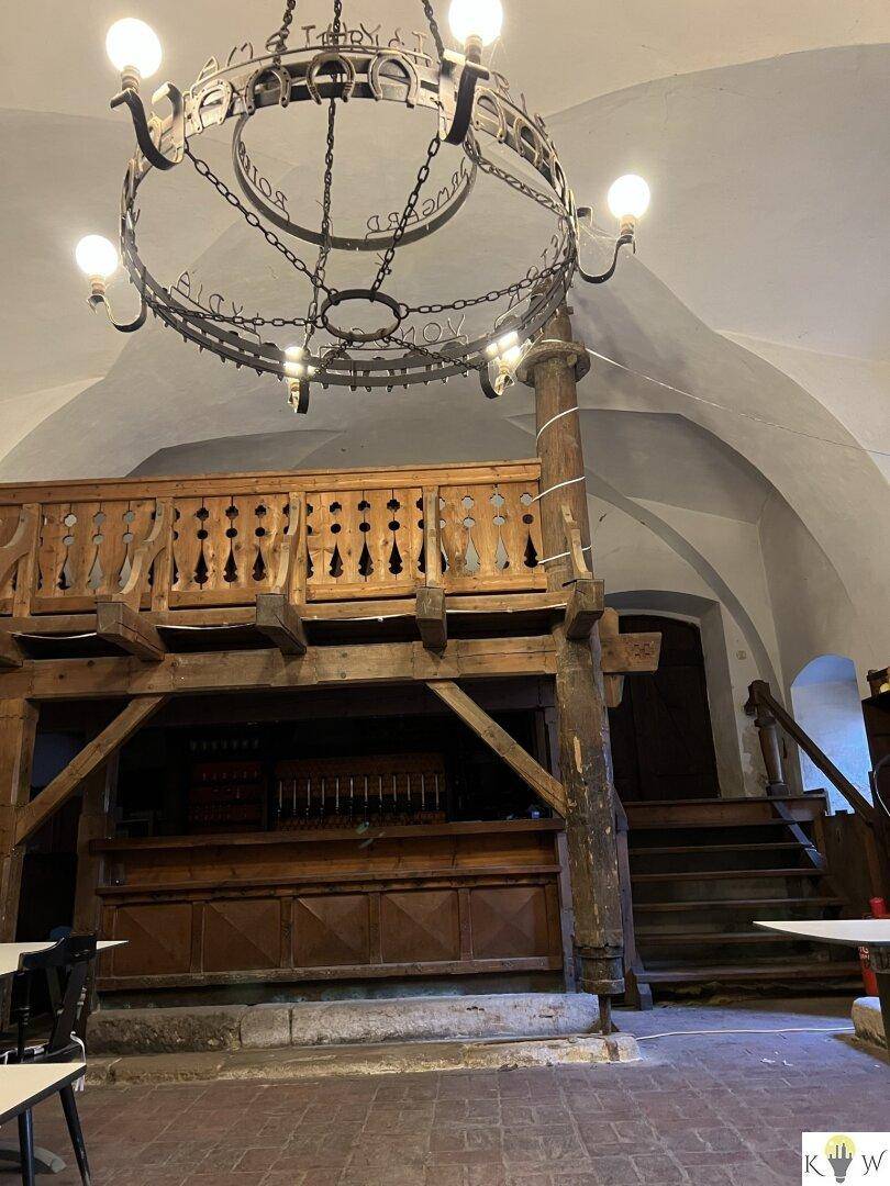Historischer Gewölberaum mit Holzbalkon, Kronleuchter und traditioneller Einrichtung, ideal für Veranstaltungen.