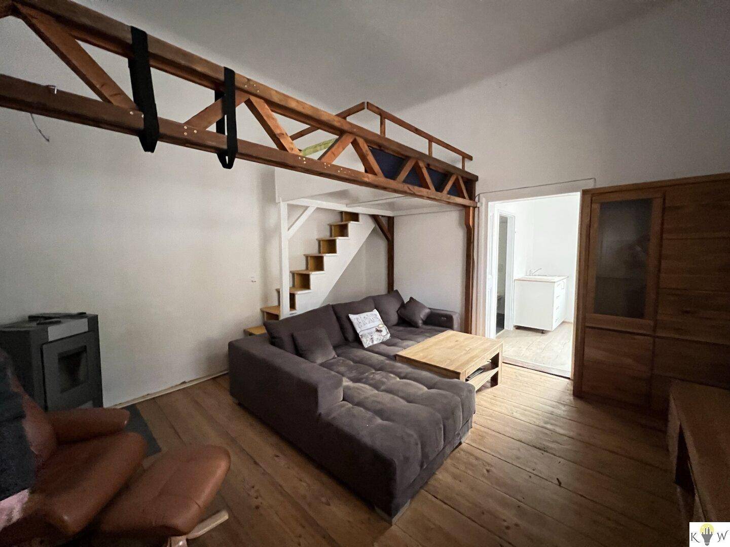 Gemütliches Wohnzimmer mit Holzboden, modernem Sofa, Holzofen und einer Galerie mit Treppe.