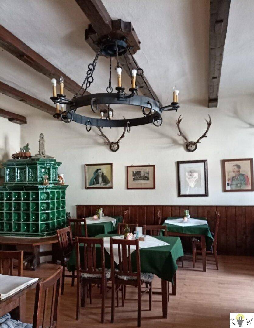 Rustikaler Essbereich mit großem grünem Kachelofen, Holzbalken und traditioneller Geweihdekoration.