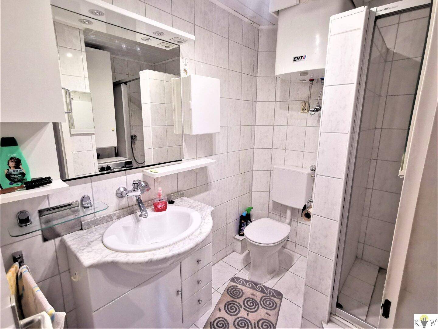 Gefliestes Badezimmer mit Waschbecken, Toilette und Duschkabine in hellem Design.
