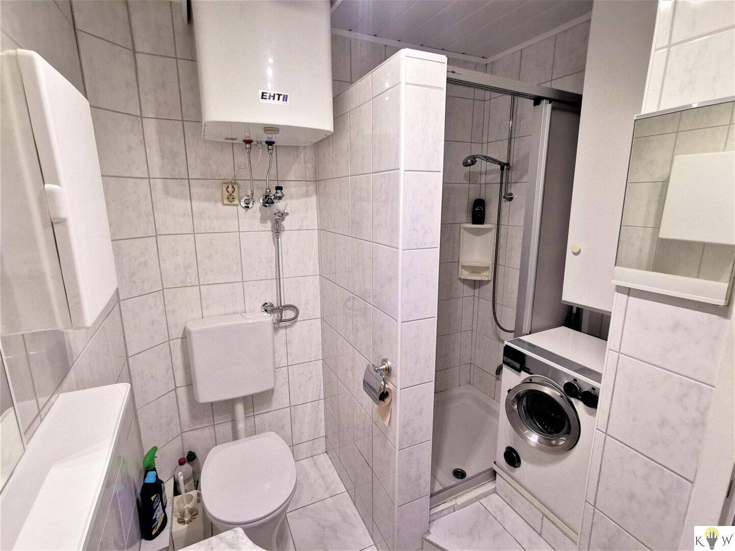 Helles Badezimmer mit Dusche, Toilette und integrierter Waschmaschine.