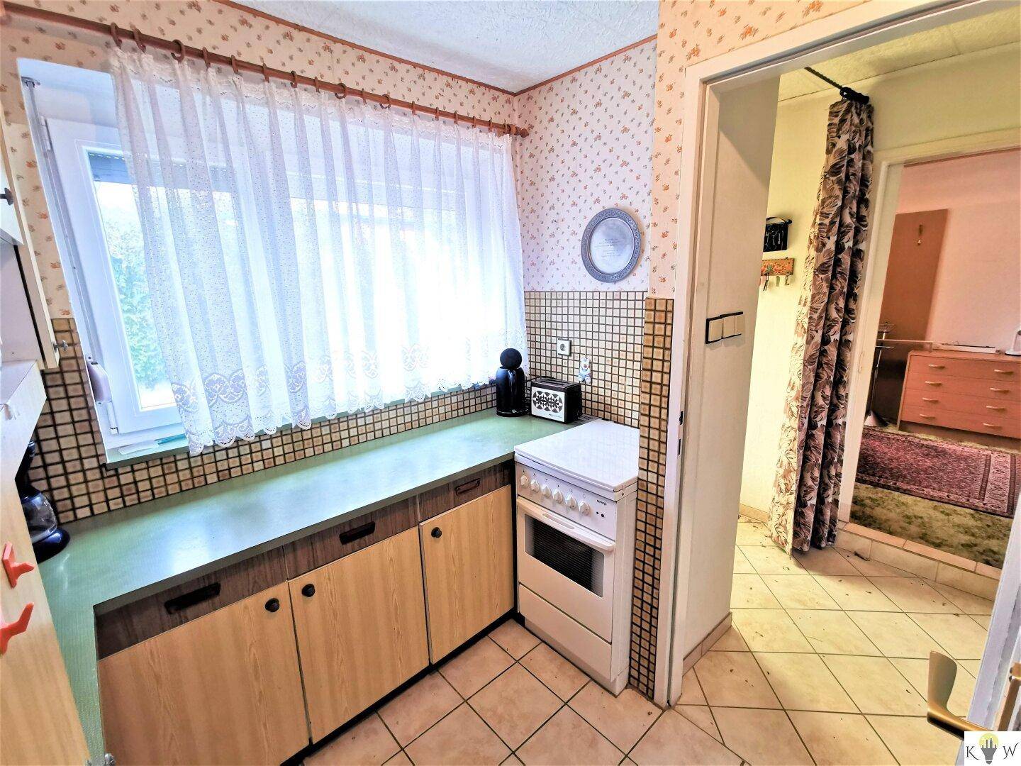 Kleine Küche mit Fenster, einfacher Ausstattung und gefliestem Boden.