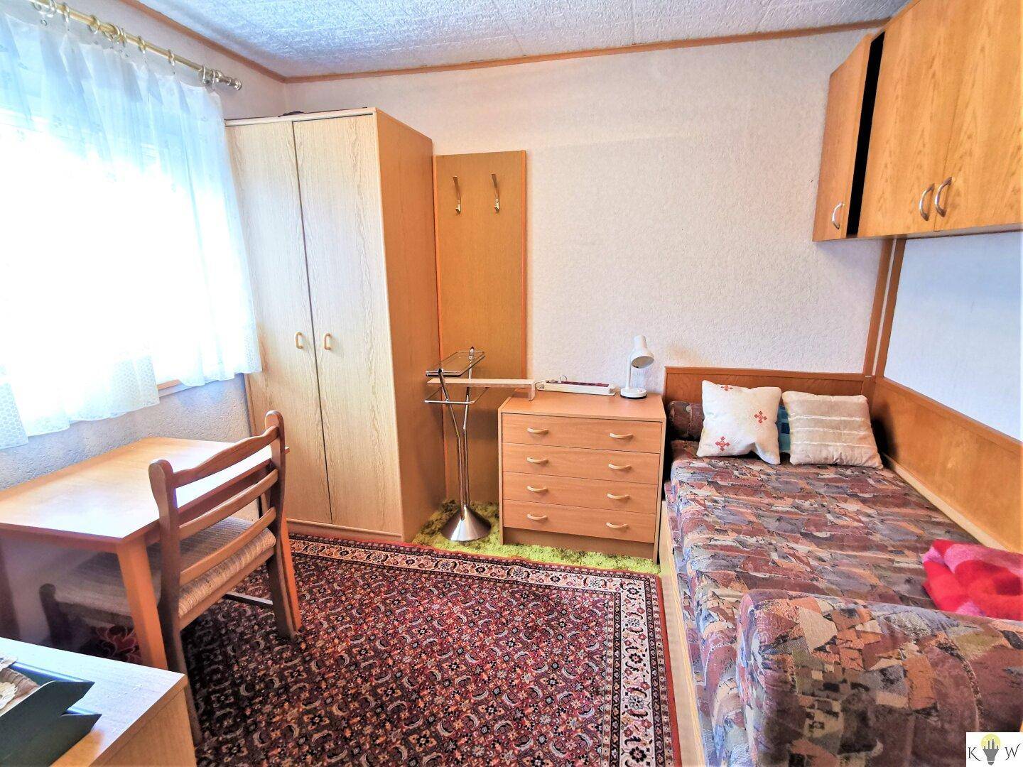 Gemütliches Schlafzimmer mit Einzelbett, Holzmöbeln und einem traditionellen Teppich.