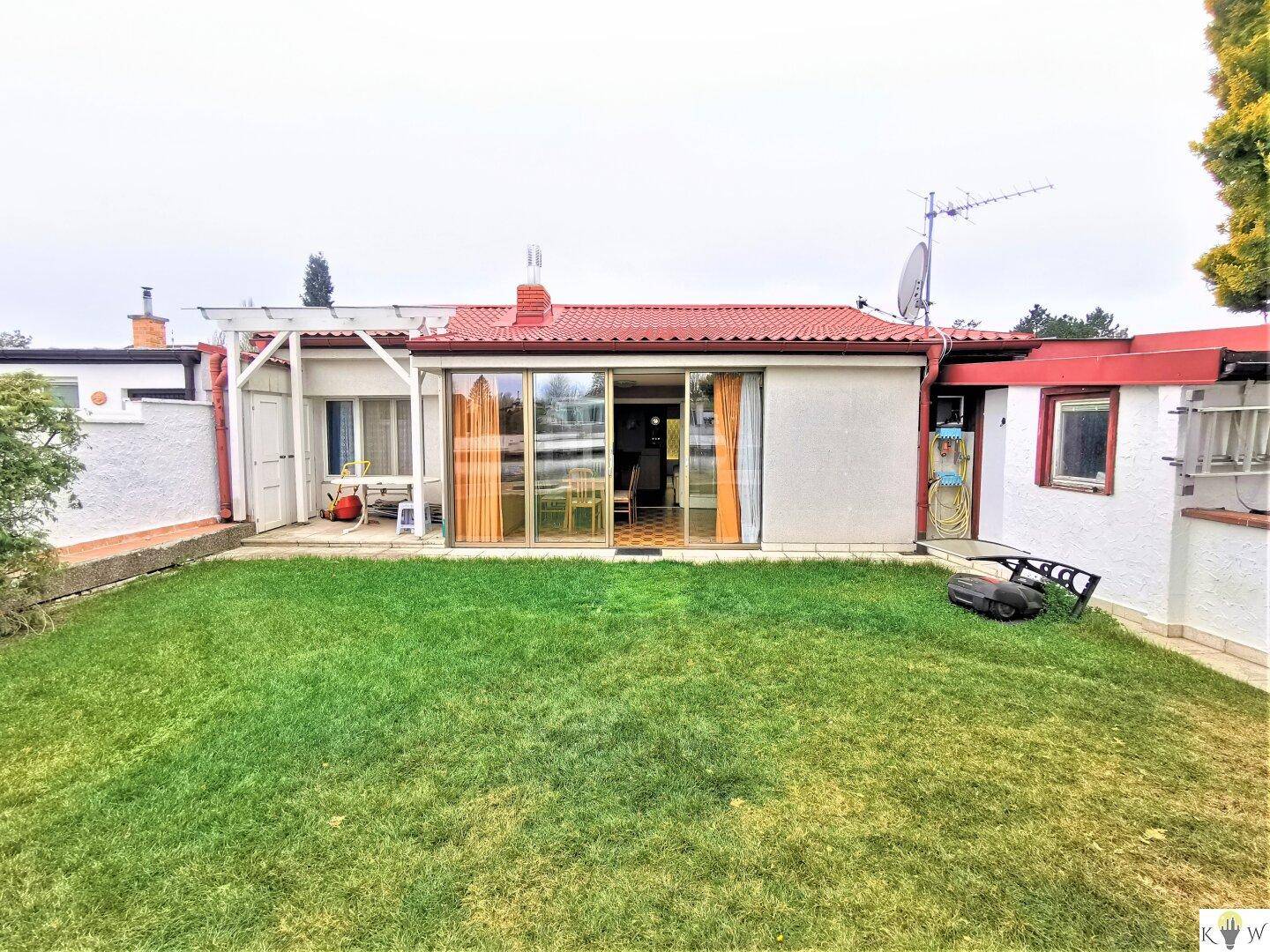 Hinteransicht des Hauses mit einer grünen Rasenfläche und großen Glasschiebetüren zur Terrasse.