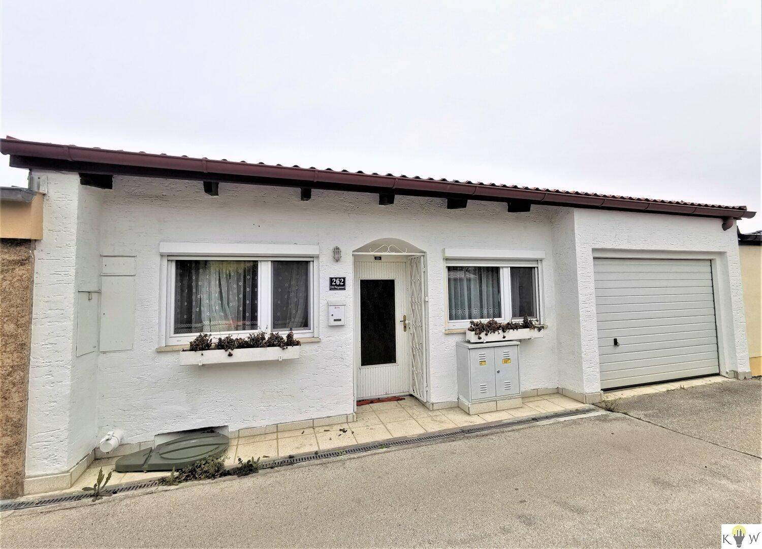 Vorderansicht des weißen Einfamilienhauses mit Garage und kleinen Blumenkästen an den Fenstern.