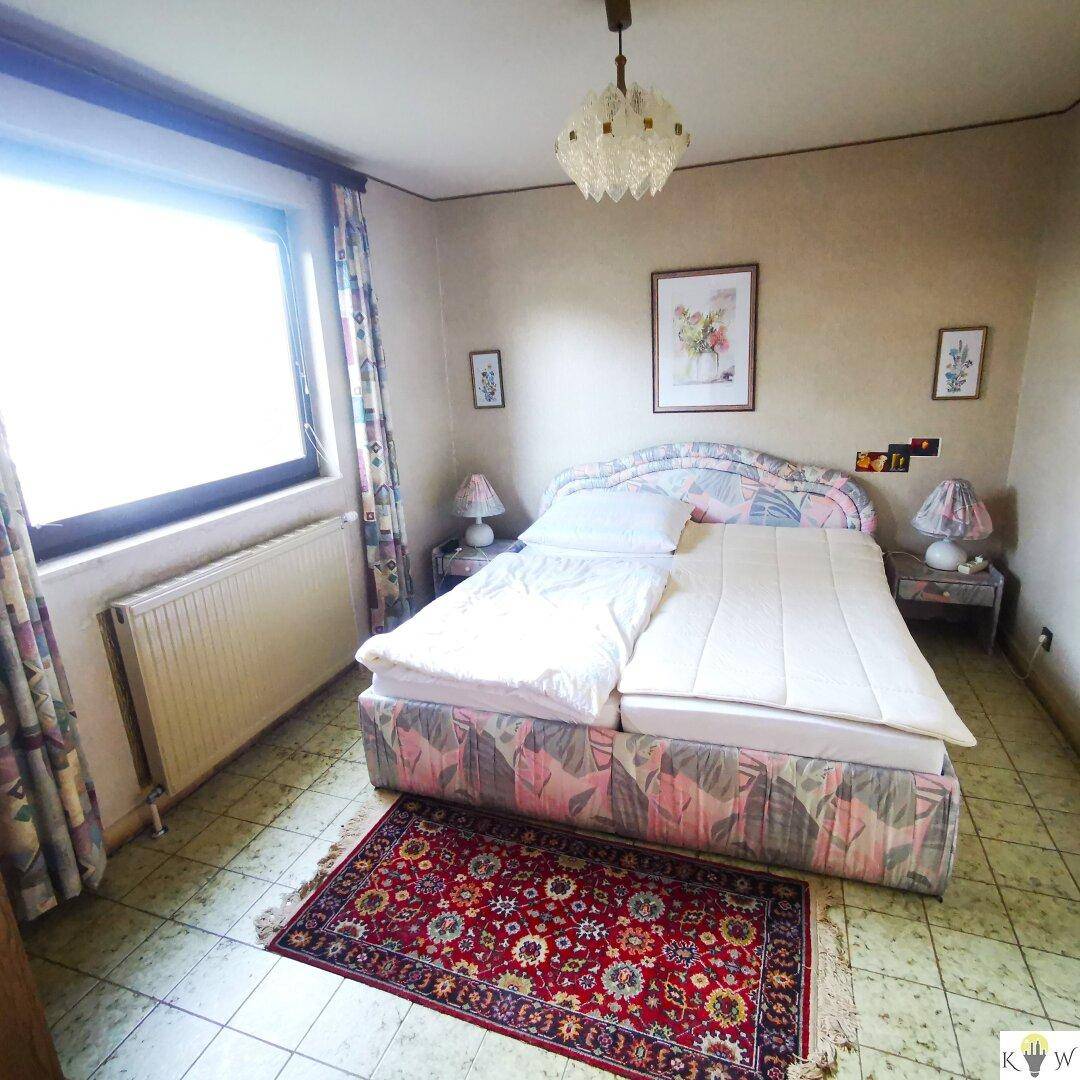 Schlafzimmer mit Doppelbett, Teppich und großem Fenster für natürliches Licht.