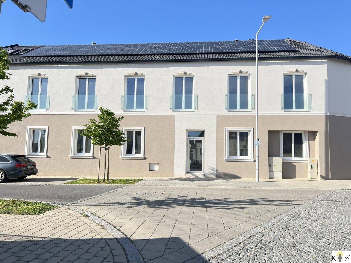 Moderne Gebäudefassade mit großen Fenstern, französischen Balkonen und Photovoltaikanlage auf dem Dach.