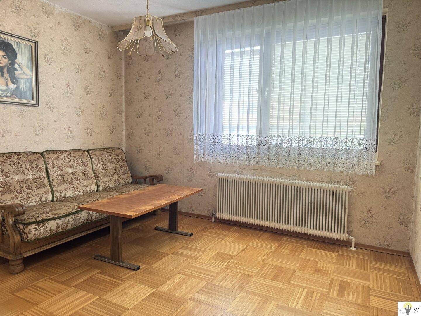 Gemütliches Wohnzimmer mit Parkettboden, floraler Tapete und traditionellem Sofa.
