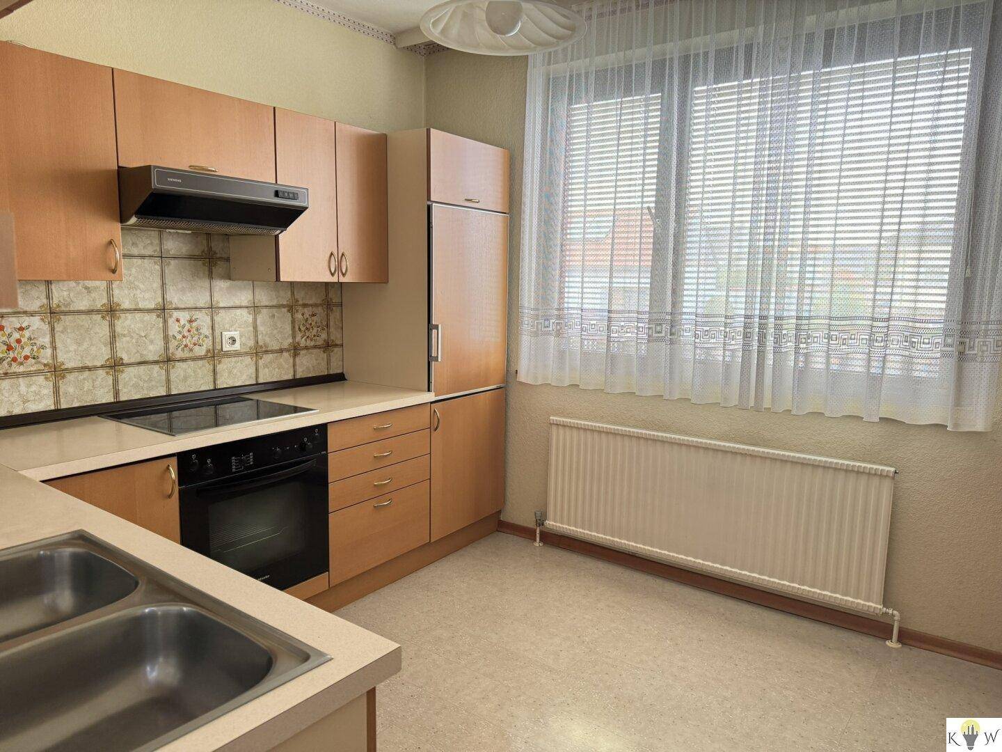 Funktionale Küche mit Holzschränken, Fliesenrückwand und Fenster.